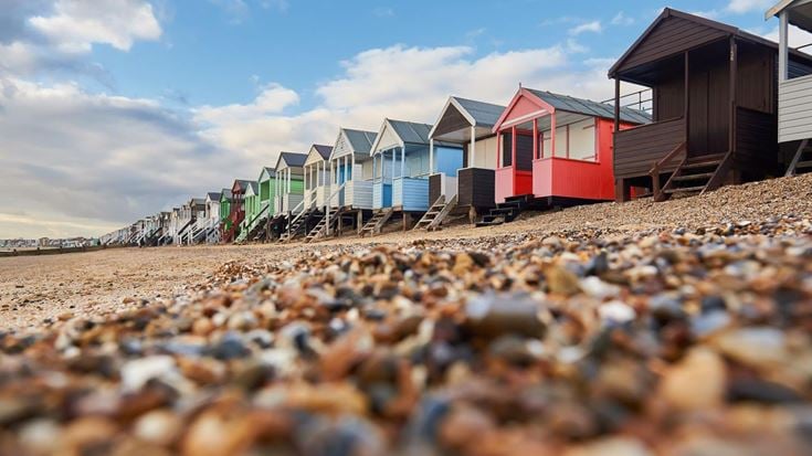A row of multicoloured beach huts on a pebble shoreline.