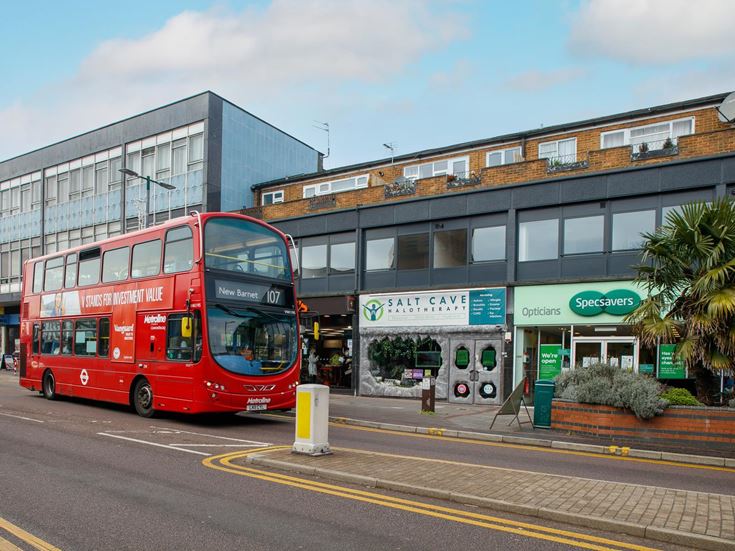 A red double decker bus parked outside local shops on Shenley Road.