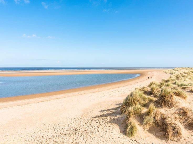 A long sandy beach along the Norfolk Coastal Path, with grass along the shoreline.