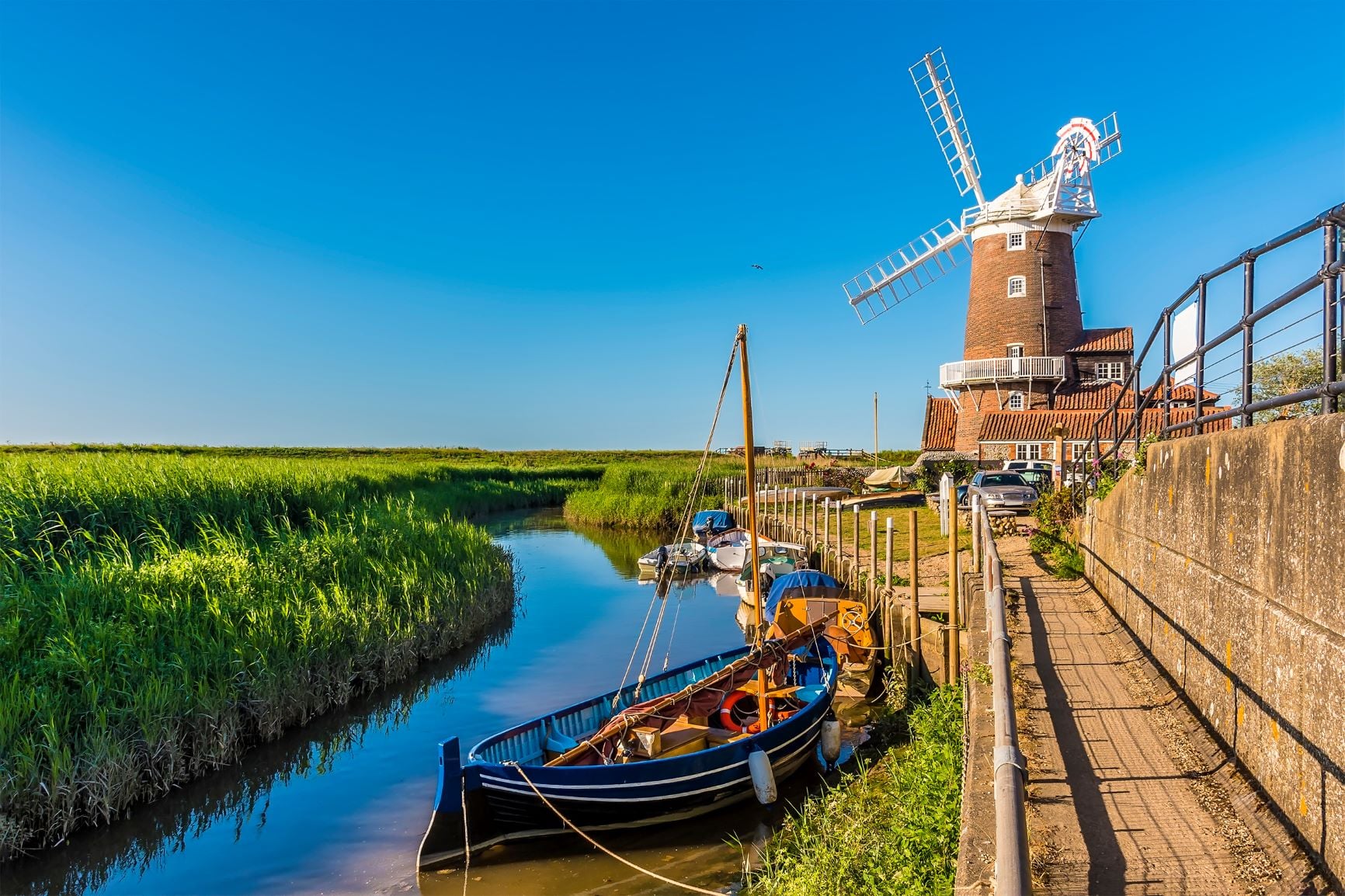 A small sailboat on the River Glaven in Cley, Norfolk, beside a windmill.