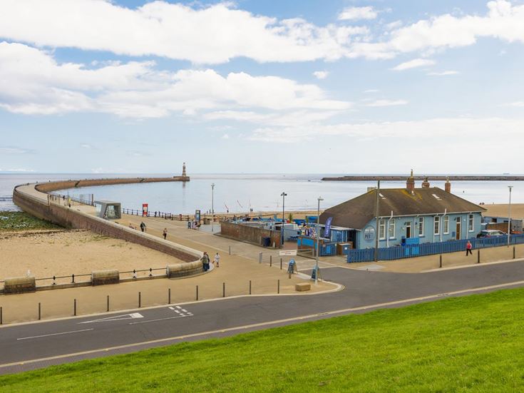 A beachfront and building in front of Roker Pier and Lighthouse.