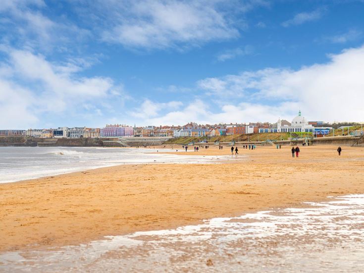 Whitley Bay beach with people walking along it and the town buildings in background.
