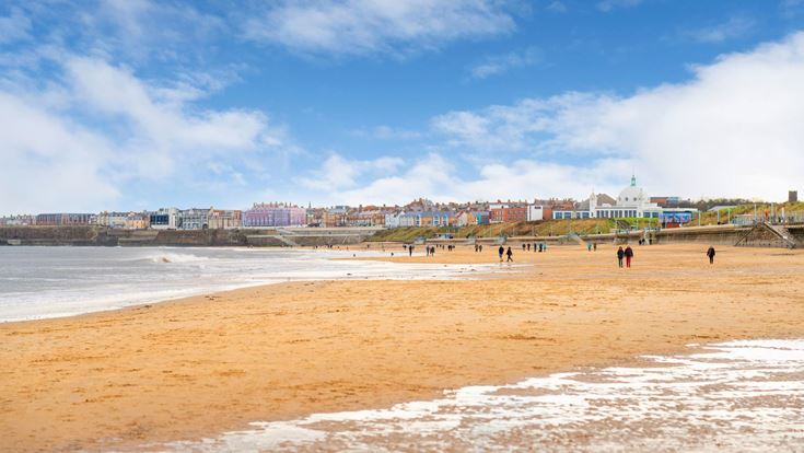Whitley Bay beach with people walking along it and the town buildings in background.
