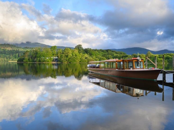 Cruise boat moored next to jetty on calm waters at Derwentwater, Lake District.