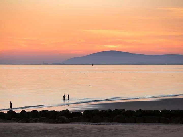 a couple of people walking on a beach with a body of water in the background
