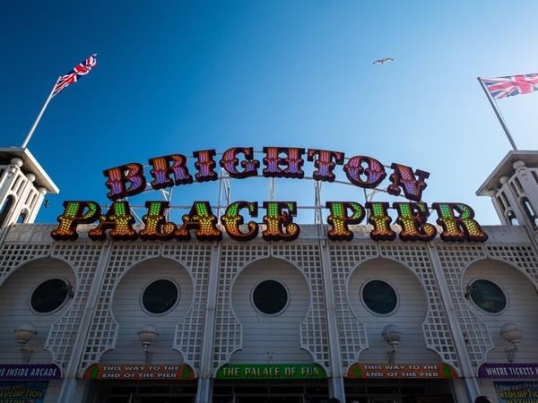 Two Union Jack flags sit on either side of a large colourful sign that reads ‘Brighton Palace Pier’.