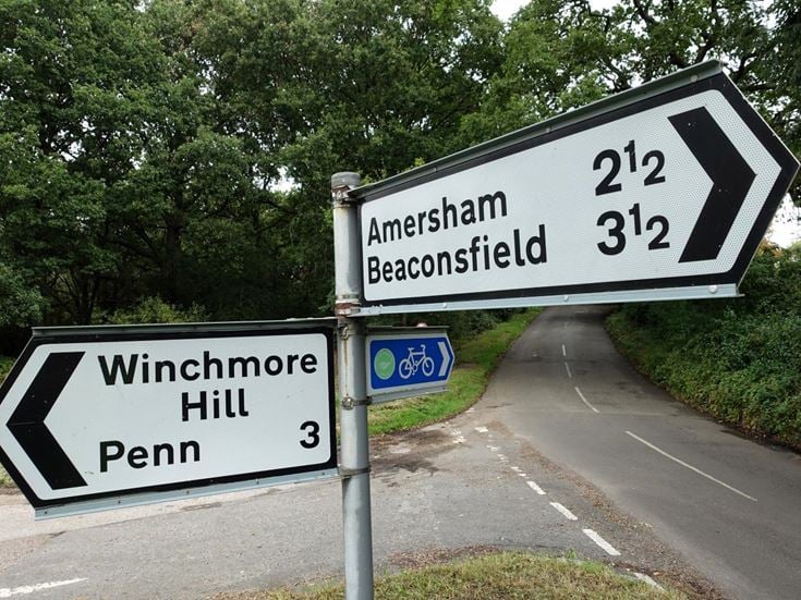 A road sign pointing to Amersham, Beaconsfield, Winchmore Hill, and Penn.