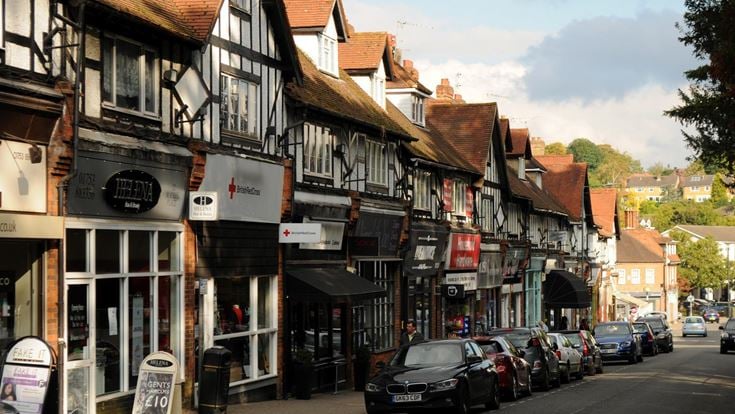 A main road with cars, lined with shops and Tudor-style buildings.