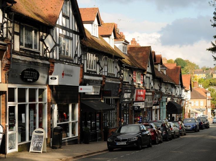 A main road with cars, lined with shops and Tudor-style buildings.