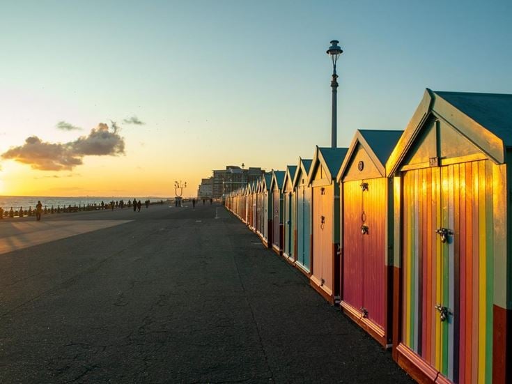Beach huts overlook the sea in Brighton during sunset.