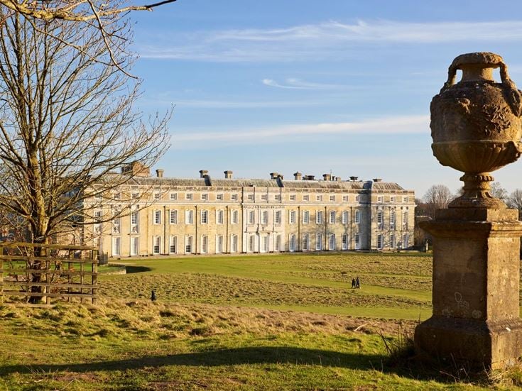 A view of the grand exterior of Petworth House over the parkland.
