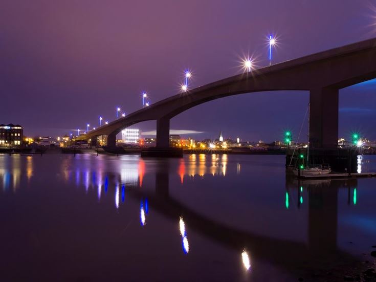 Itchen Bridge over still water in Southampton at night, with light reflected on the water.