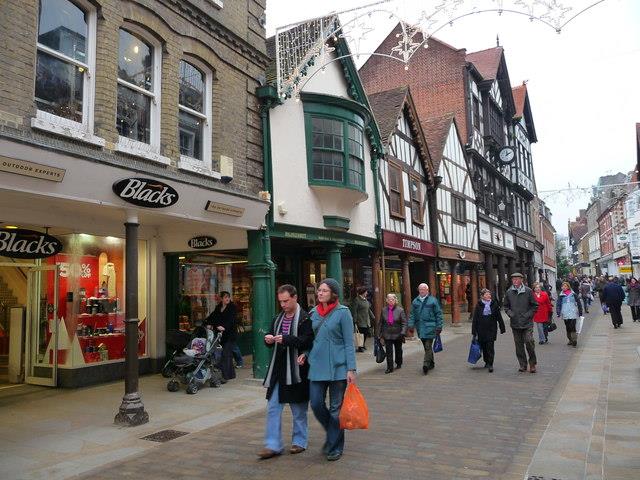 People walking down the high street in Winchester, which is lined with several shops in historic buildings.