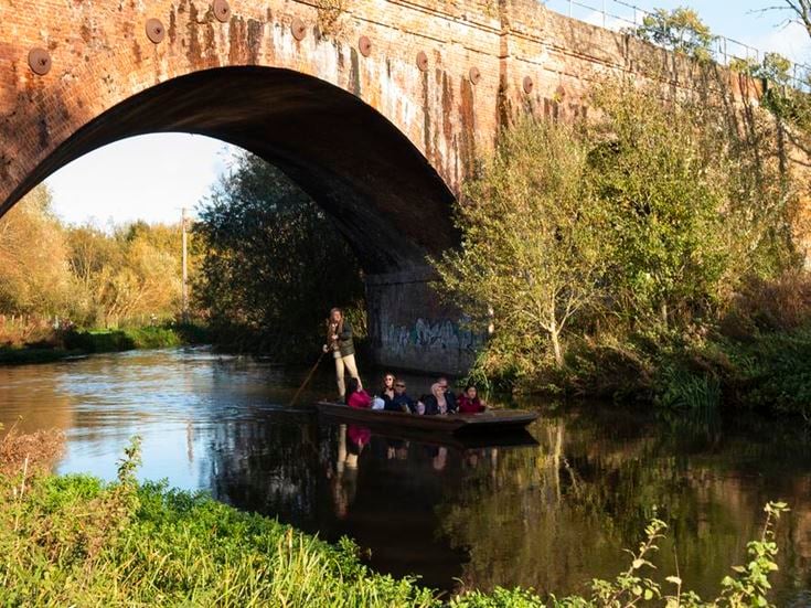 A group of people on a punt on the Great Sour river under a bridge.