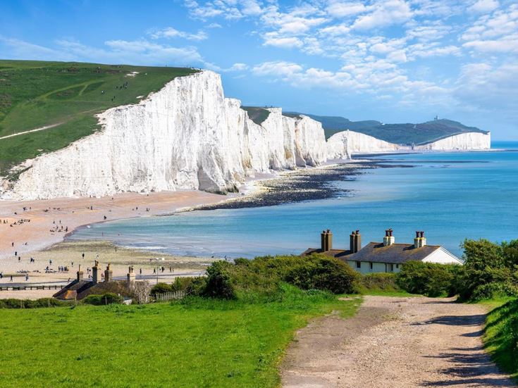 A path leading to buildings and beach with the White Cliffs of Dover in the background.