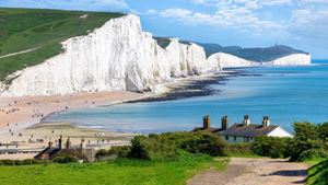 A path leading to buildings and beach with the White Cliffs of Dover in the background.