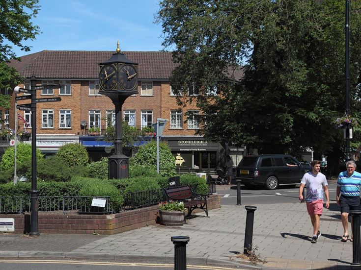 A couple of people walk down the high street next to the Millennium Clock, Cobham.