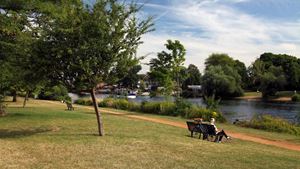 A senior woman sits on a bench by the River Thames.
