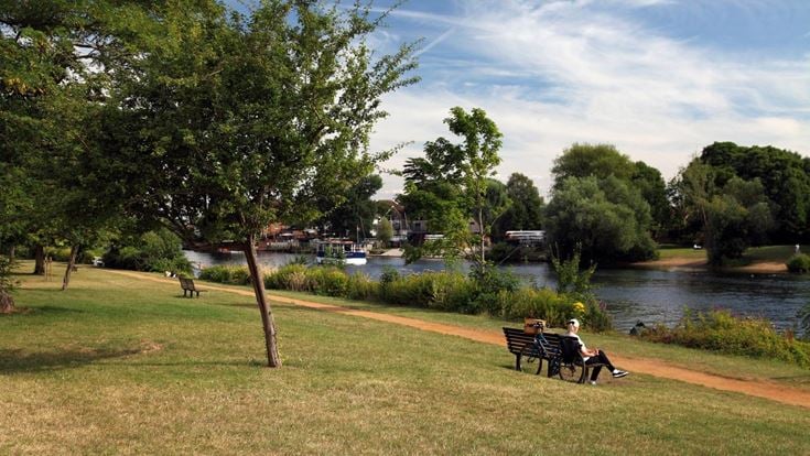 A senior woman sits on a bench by the River Thames.