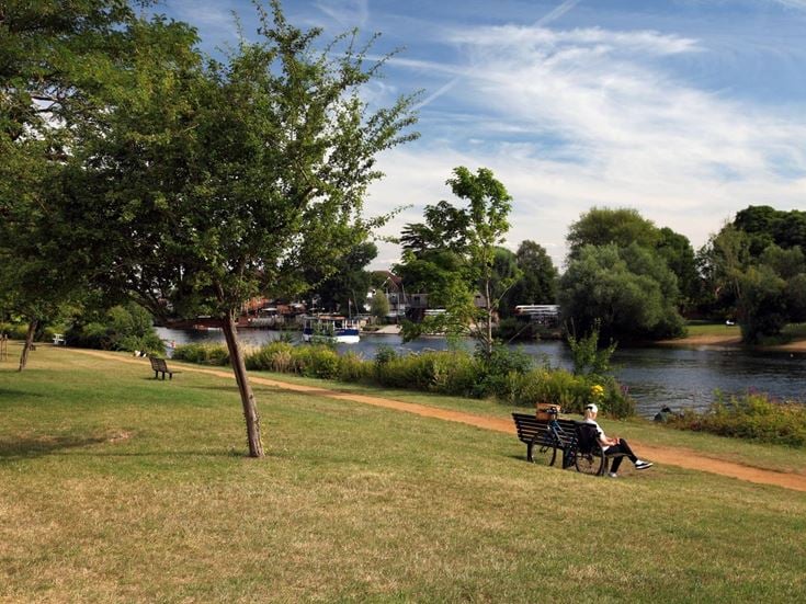 A senior woman sits on a bench by the River Thames.