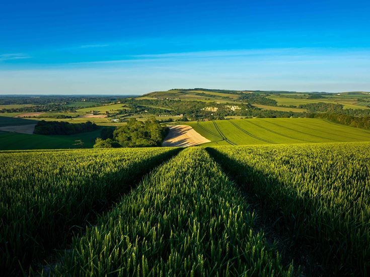 A green field surrounded by rolling panoramic hillscapes set against a cloudless sky.