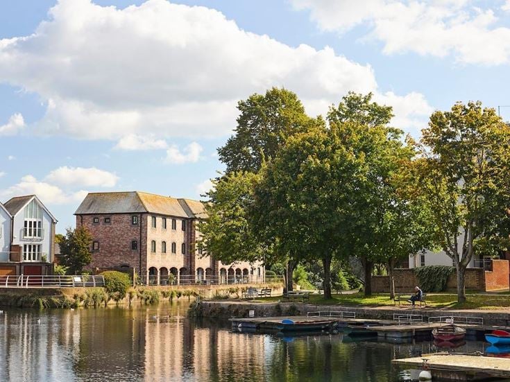 A scenic view over a waterway in Chichester, with historic red brick buildings and trees in the background