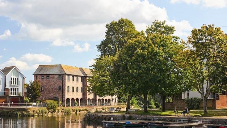 A scenic view over a waterway in Chichester, with historic red brick buildings and trees in the background