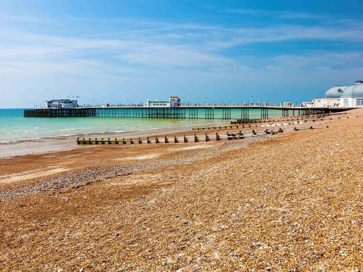 A pebbly beach and sea front in the foreground with Worthing Pier in the distance