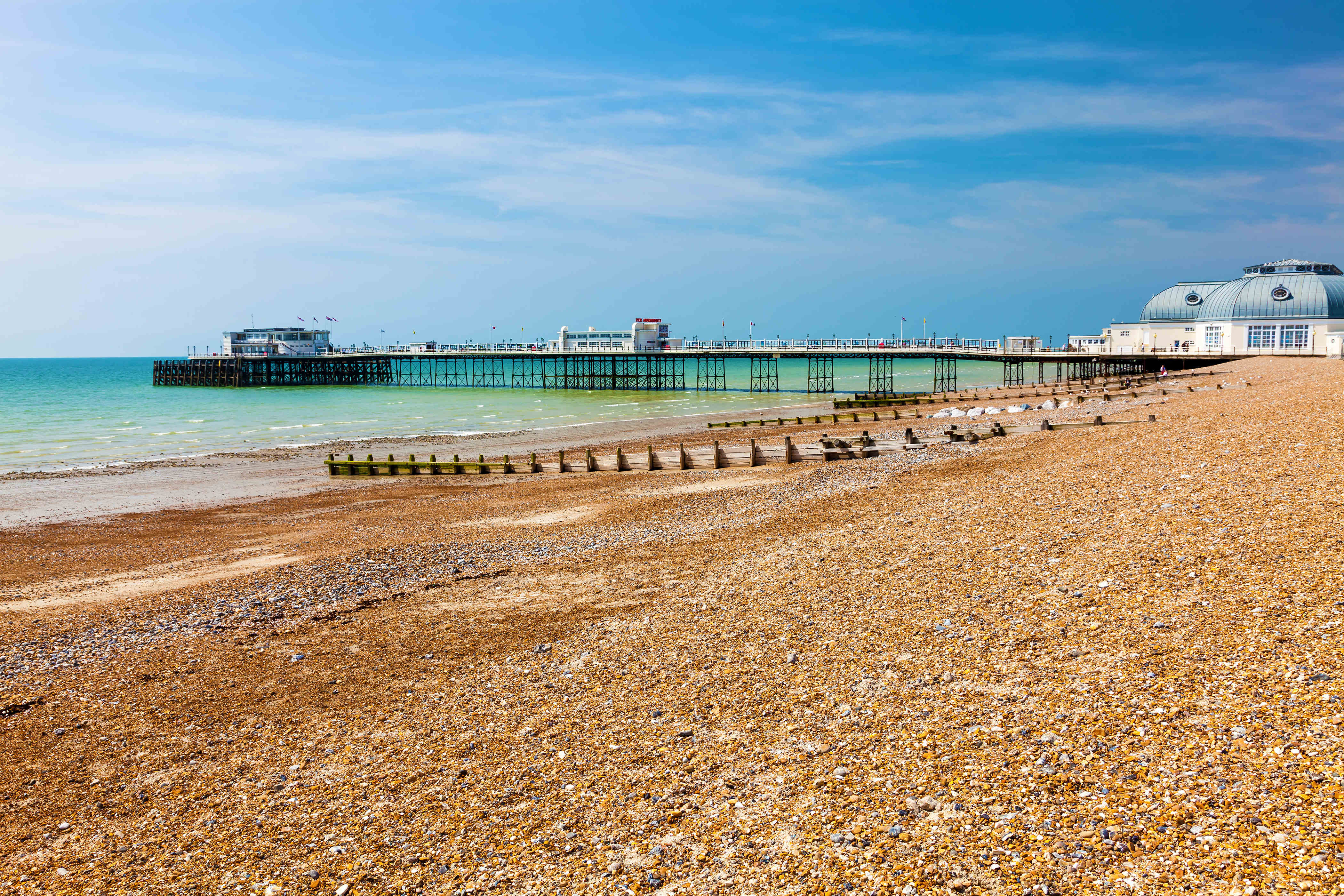 A pebbly beach and sea front in the foreground with Worthing Pier in the distance