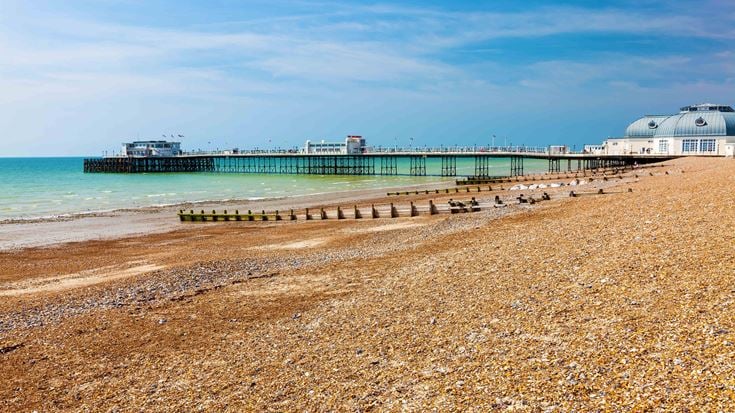 A pebbly beach and sea front in the foreground with Worthing Pier in the distance