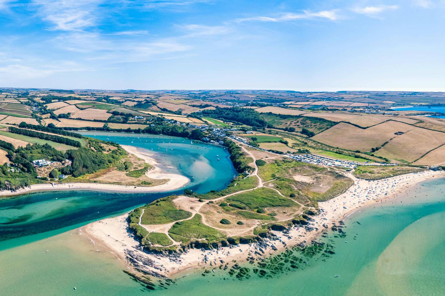 An aerial view of one of Devon’s many coasts, with fields and rolling green hills in the surroundings.