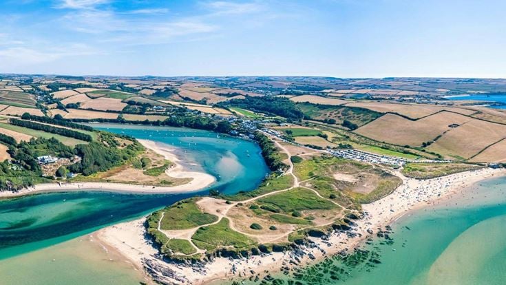 An aerial view of one of Devon’s many coasts, with fields and rolling green hills in the surroundings.