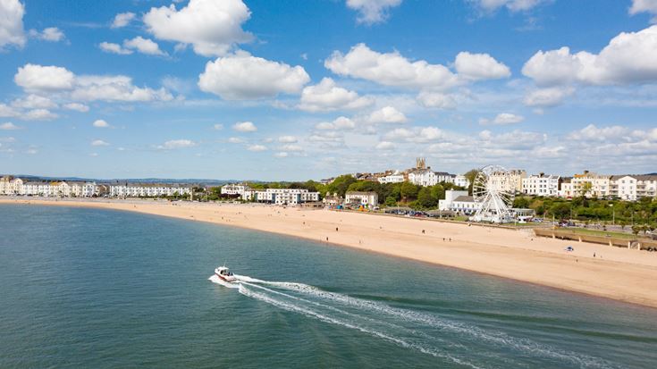 The seafront in Exmouth, with a boat and a green fields across the bay