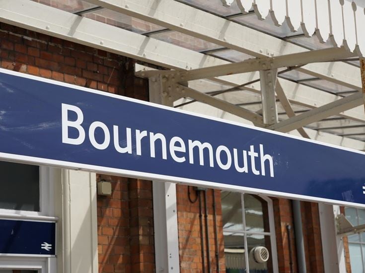 A blue 'Bournemouth' railway station sign hanging from a platform canopy.