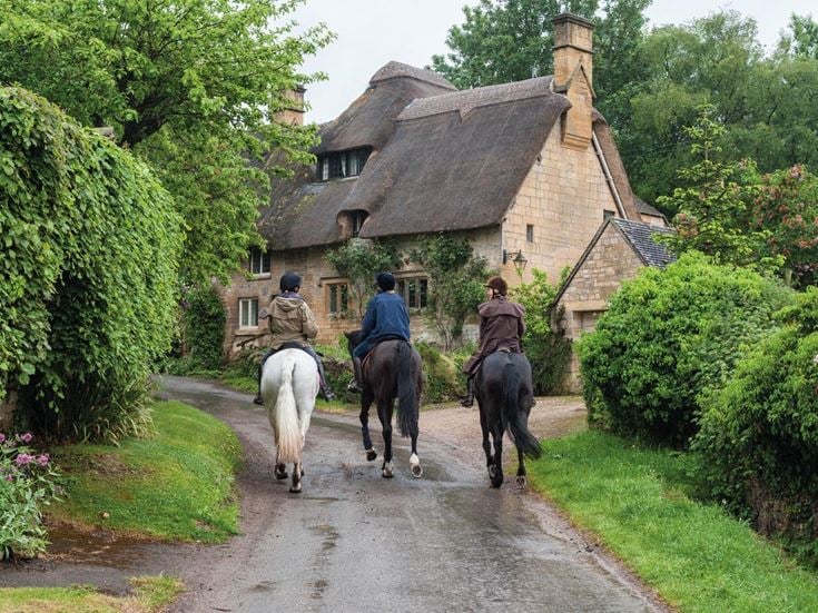 Three people riding horses along a country lane in Stow-on-the-Wold.