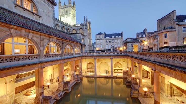 The Roman Baths in Bath at Dusk with Bath Abbey in background lit up.