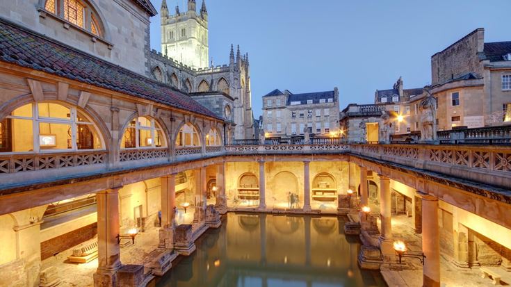 The Roman Baths in Bath at Dusk with Bath Abbey in background lit up.
