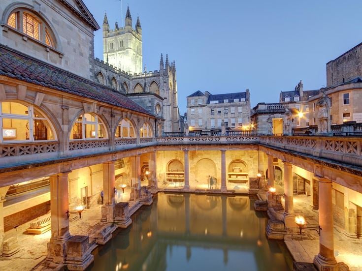 The Roman Baths in Bath at Dusk with Bath Abbey in background lit up.