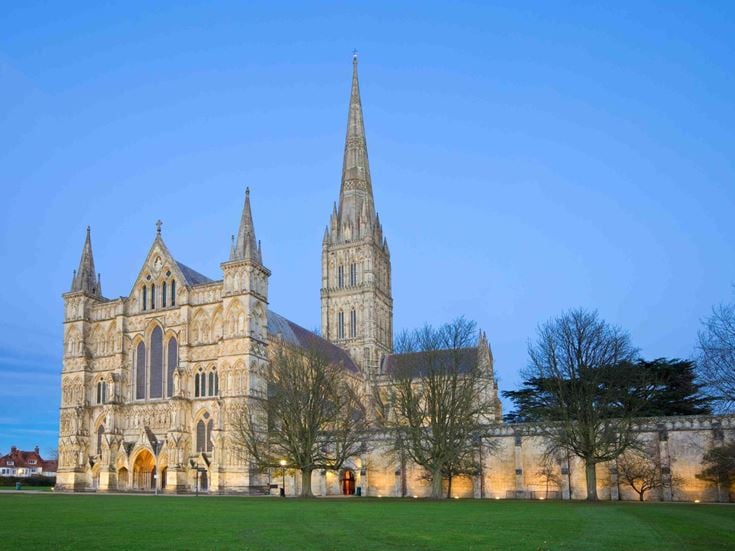Exterior view across a green in front of Salisbury Cathedral at dusk.