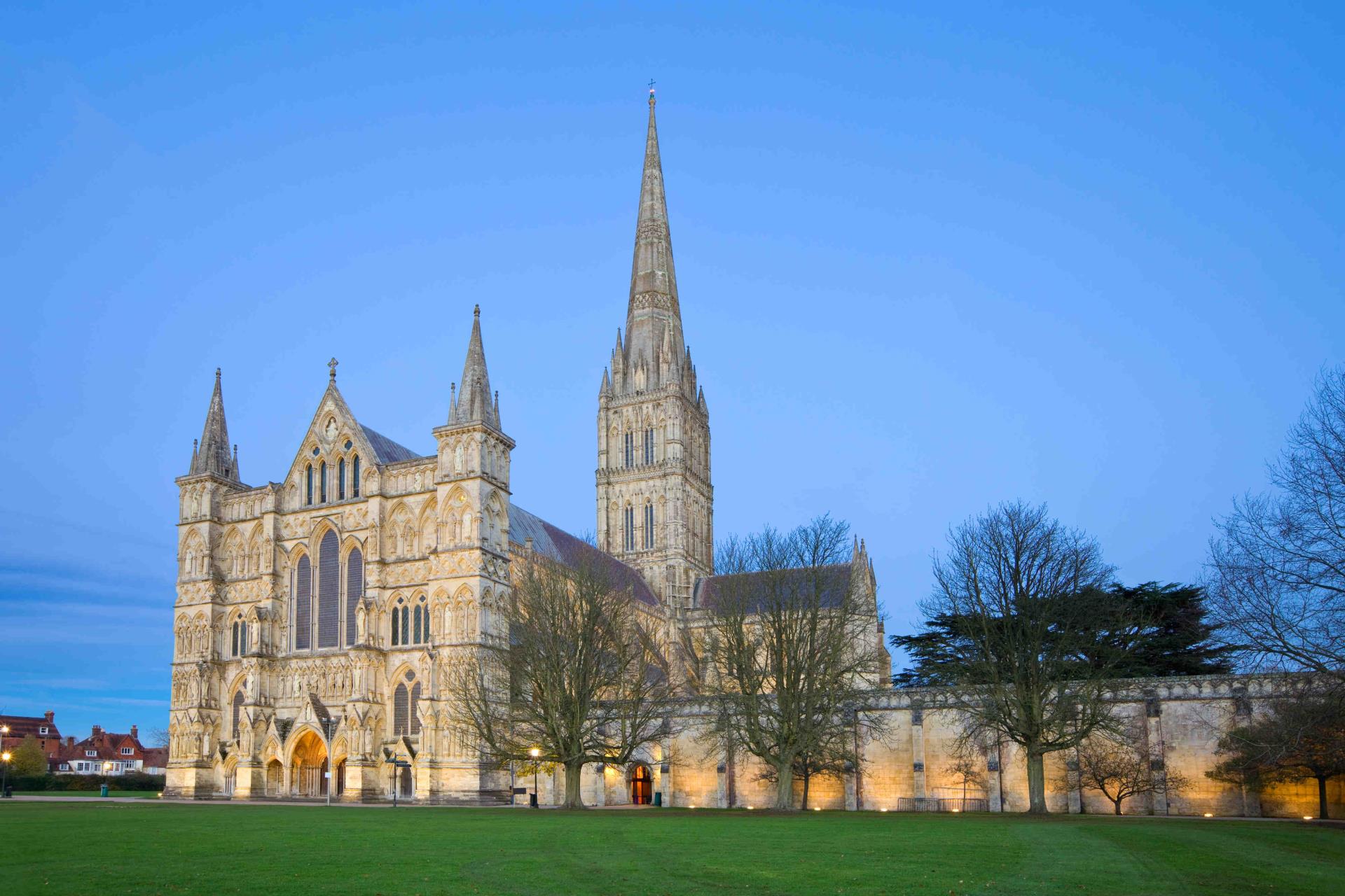 Exterior view across a green in front of Salisbury Cathedral at dusk.