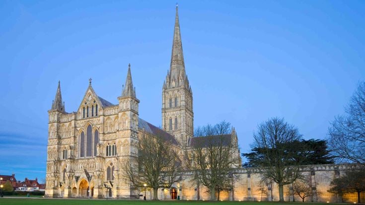 Exterior view across a green in front of Salisbury Cathedral at dusk.
