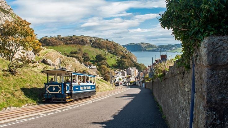 A tram coming up a hill with rolling hills and coast in the background.
