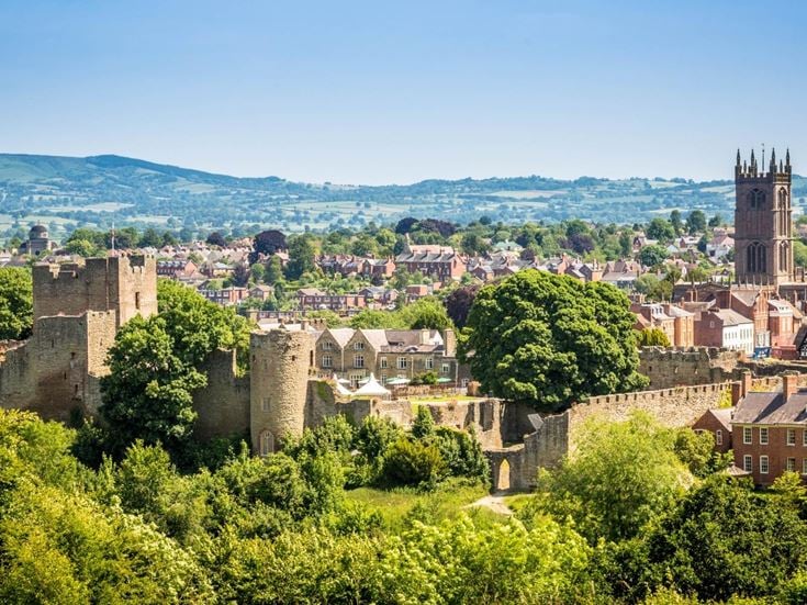 An aerial view of Ludlow Castle and surround town buildings and rolling hills in Shropshire.