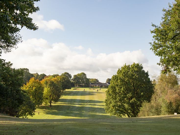 Part of the golf course at Market Drayton with large green trees in the background.