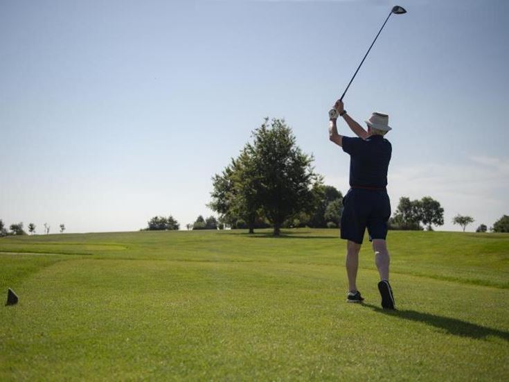 A retired man watches his golf ball travel after taking a swing with his club.