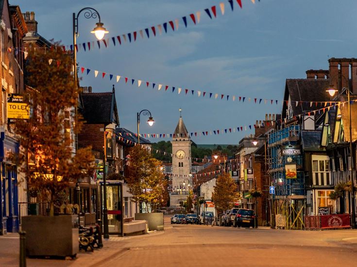 a street with buildings, trees on the side and bunting at dusk
