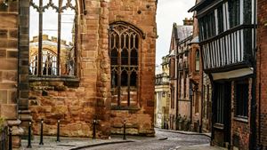 A cobblestone street between the ruins of Coventry Cathedral and a historic building.
