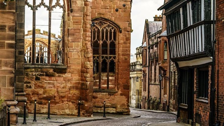 A cobblestone street between the ruins of Coventry Cathedral and a historic building.