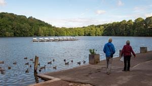 Two retirees walk alongside water populated with ducks in Boldmere Gate.