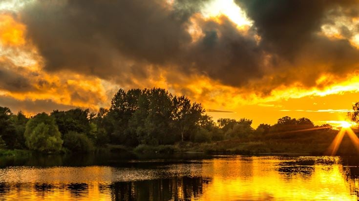 a body of water with trees and a sunset in the background